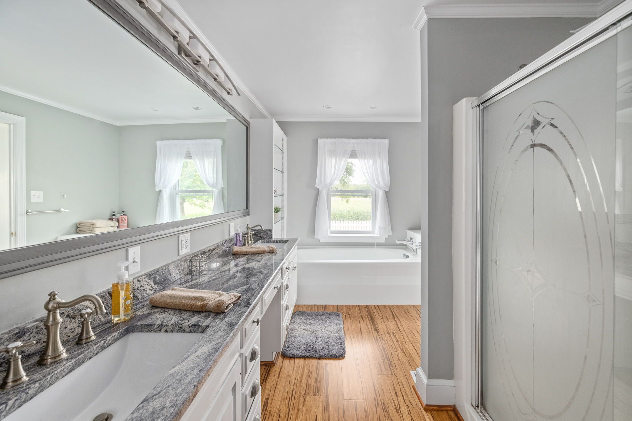 A modern bathroom with a large mirror, a marble countertop, a bathtub, and a shower area.