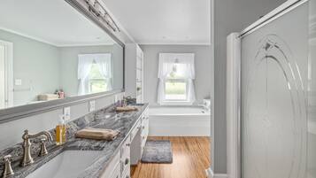 A modern bathroom with a large mirror, a marble countertop, a bathtub, and a shower area.
