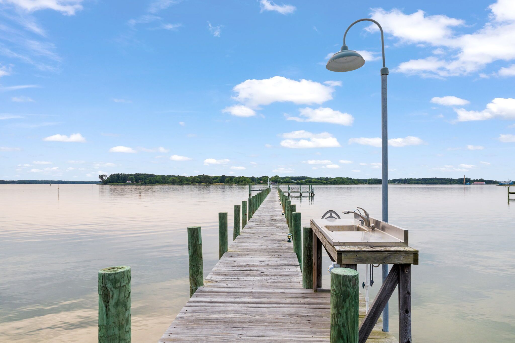 Eine hölzerne Pier, die sich über ruhiges Wasser erstreckt, mit einem Metall-Laternenpfosten und einem Waschbecken am Ende.