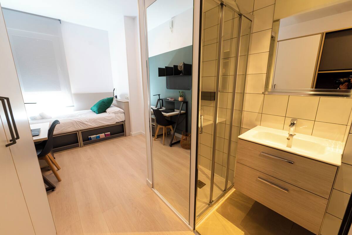 Camera da letto moderna con letto, scrivania e cabina doccia in vetro.