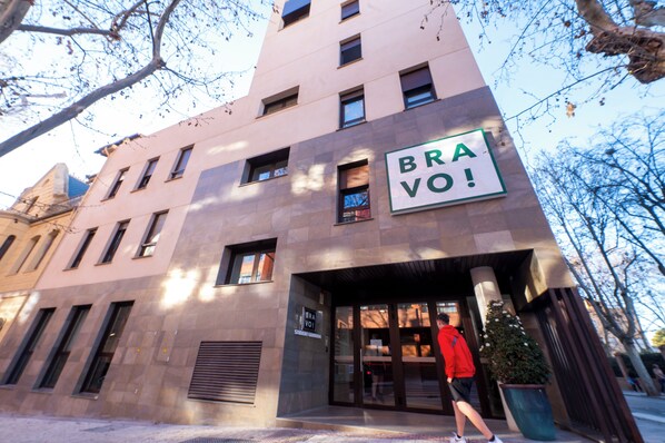 A building with a sign reading "BRAVO!" and a person in a red jacket walking towards the entrance. - Bravo Students Granada - Campus Accommodation - Campus Accommodation (Granada)