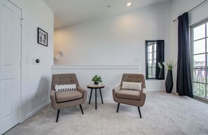A room with two armchairs, a small table with a plant, a window with curtains, and a door. - Midtown Urban Retreat | 2story 1BD/1.5BA Apartment (Houston)