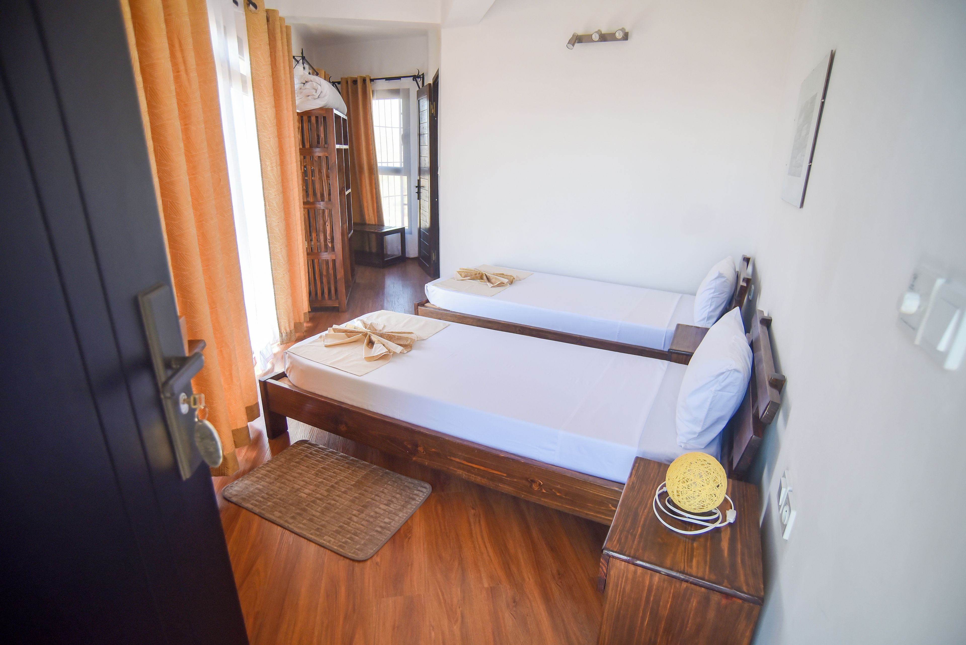 A room with two wooden beds, a small table with a woven basket, and a door with a curtain.
