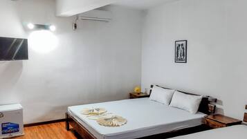 A hotel room with a bed, a bedside table, a wall-mounted TV, an air conditioner, and a framed picture on the wall.