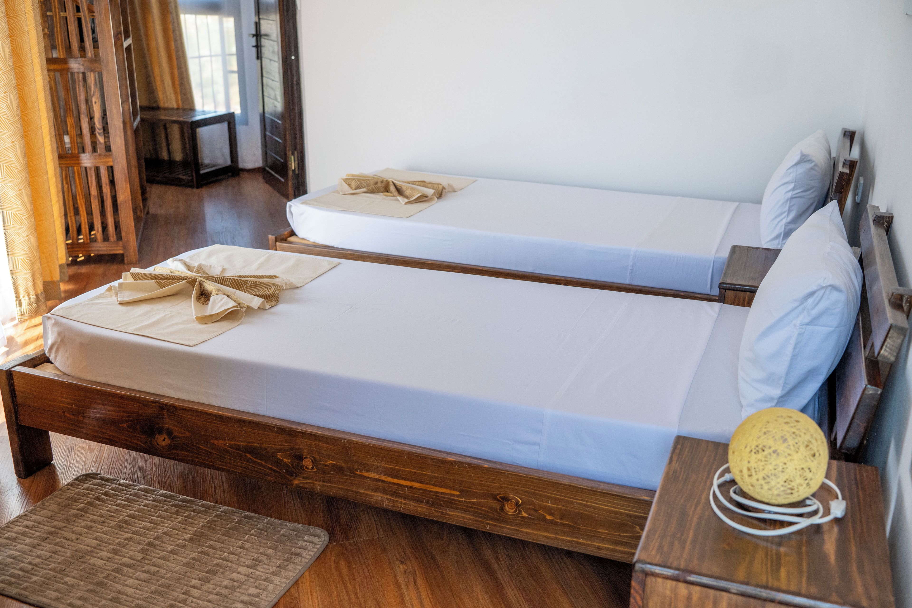 A double bed with a wooden frame and white linens, a bedside table with a lamp, and a wooden floor.