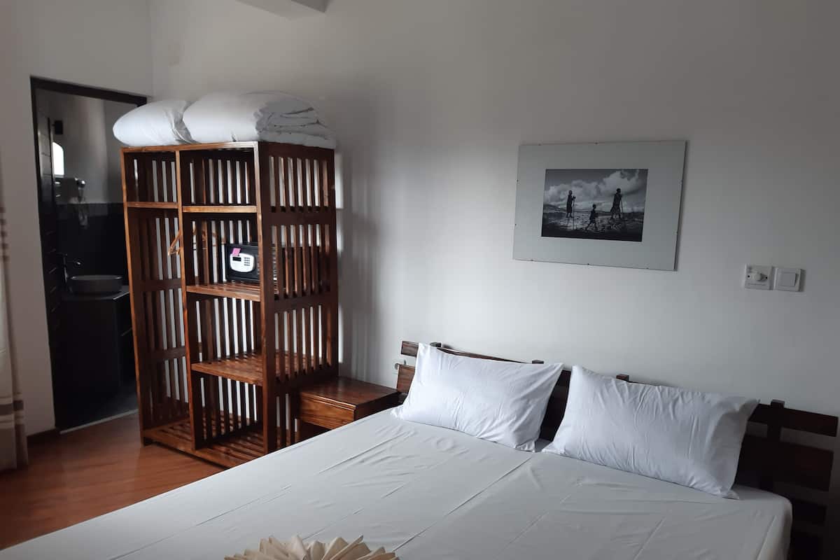 Quarto com cama grande, guarda-roupa de madeira, quadro emoldurado na parede e banheiro visível através de uma porta aberta.