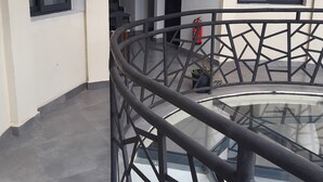 A balcony with a glass railing, a fire extinguisher, and a view of the interior. - Hôtel H1 Fianarantsoa (Fianarantsoa)