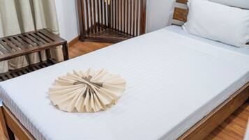 Una cama bien tendida con una toalla doblada en el centro, un cabecero de madera y una mesita de noche de madera con una lámpara.