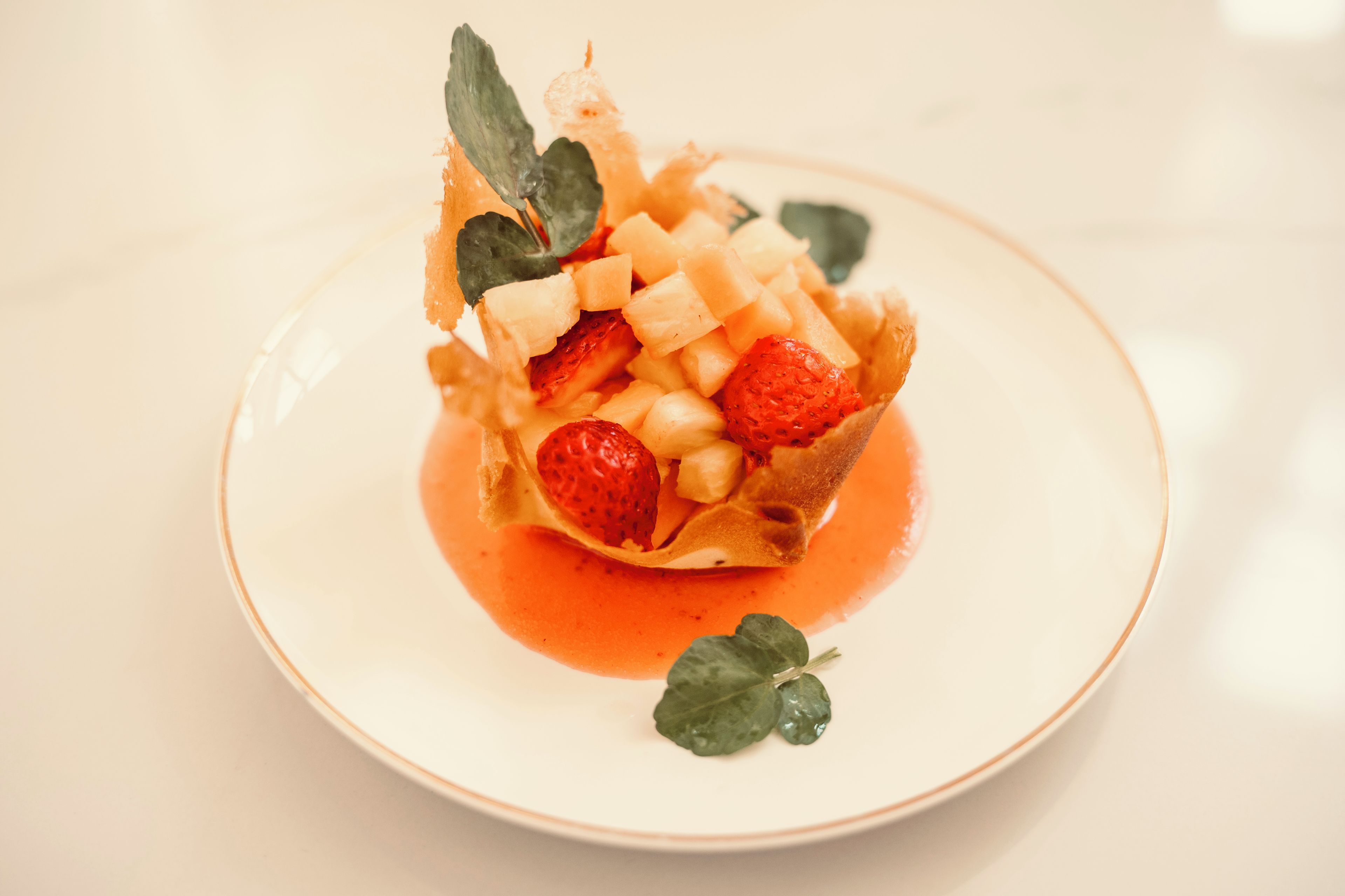 Postre en un plato con fresas, melón y salsa.