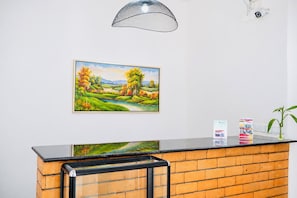 A reception desk with a brick counter, a landscape painting, a security camera, and a plant. - Hôtel H1 Fianarantsoa  (Fianarantsoa)