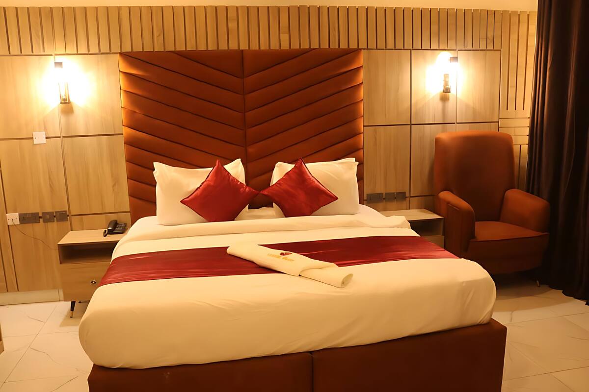 Camera d'albergo con un letto grande, una testiera in legno, due comodini, una sedia e luci a parete.