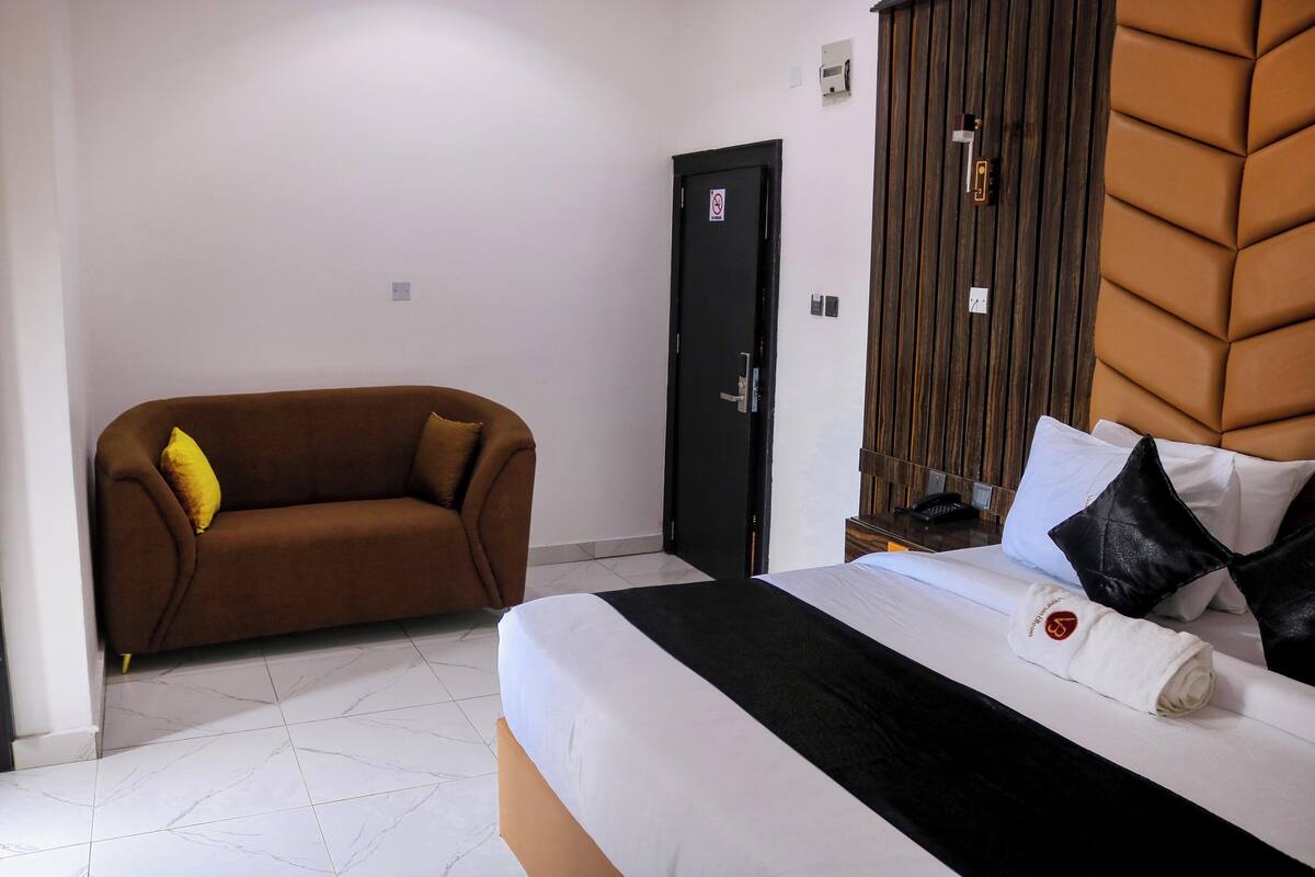 Una camera d'albergo con un letto, un divano marrone e una testiera in legno.