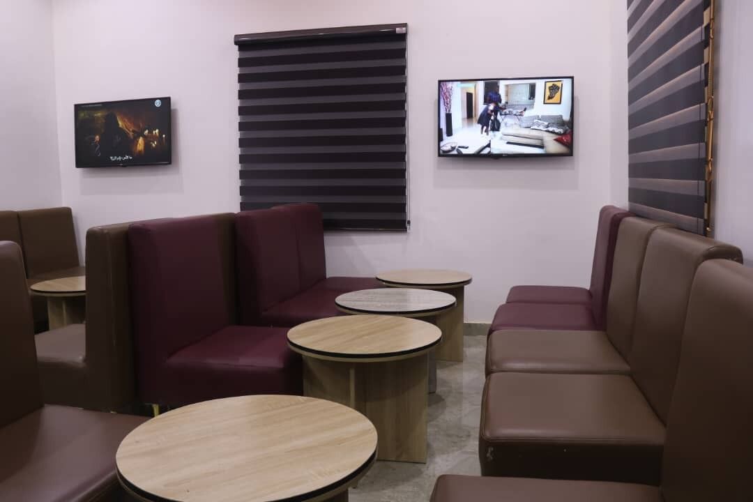 Un área de descanso moderna con asientos de cuero, pequeñas mesas redondas y dos televisores de pantalla plana montados en las paredes.