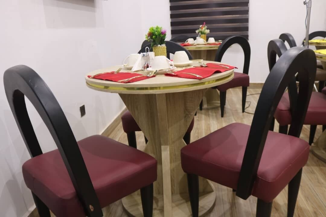 Comedor con mesas redondas, sillas tapizadas en rojo y una pequeña planta decorativa sobre las mesas.