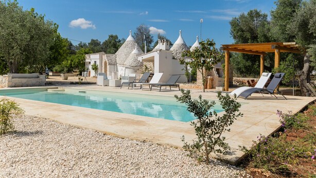 Una piscina con sillas de descanso, una pérgola y edificios de piedra con techos cónicos.
