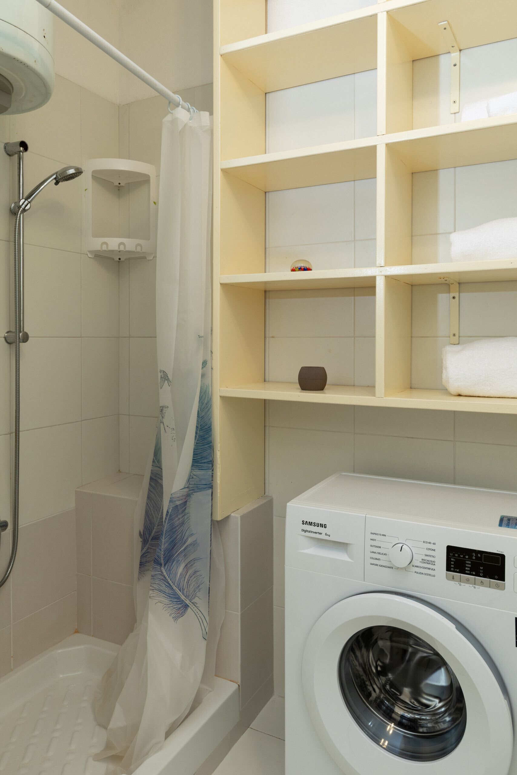 A bathroom with a shower, a washing machine, and shelves with toiletries.