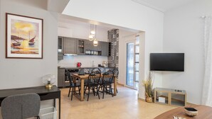 Une cuisine moderne avec des meubles de couleur grise, une table à manger en bois et un téléviseur fixé au mur.