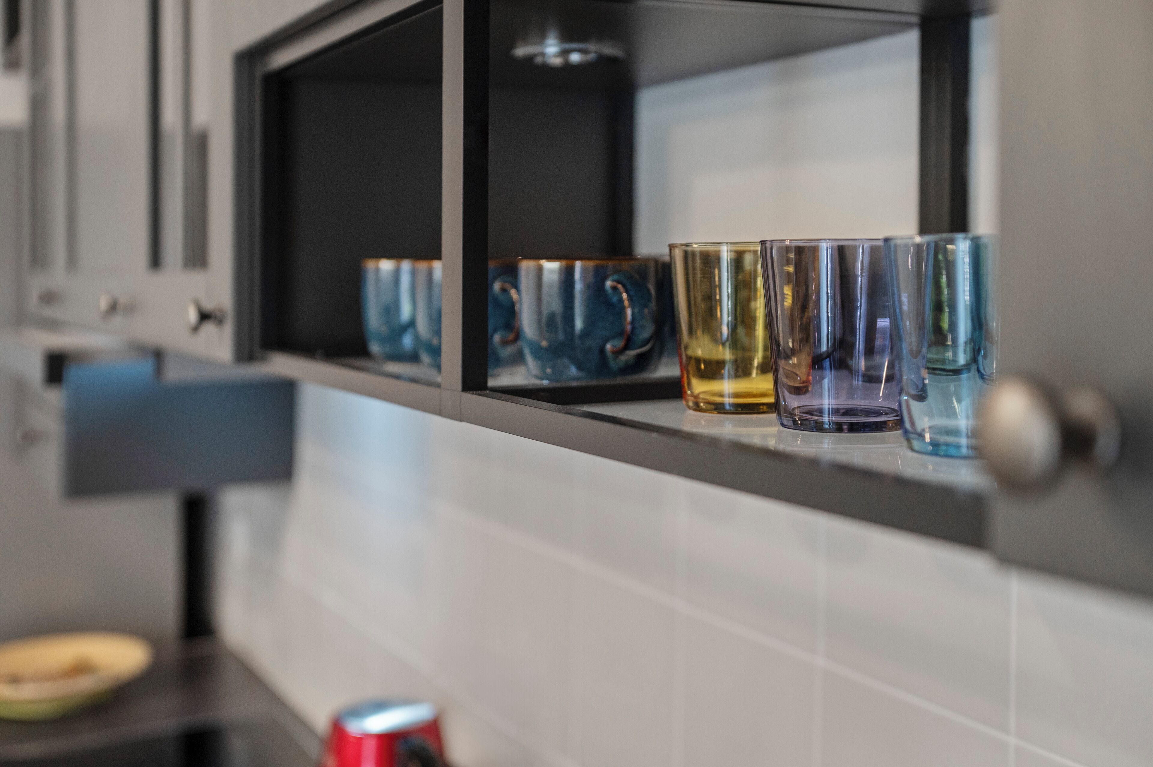 Una cuina amb una estant que conté diversos vasos de vidre i una llauna.