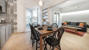 Un coin repas avec une table et des chaises en bois, une cuisine avec un crédence décorée, et un espace de vie avec un canapé et des coussins.