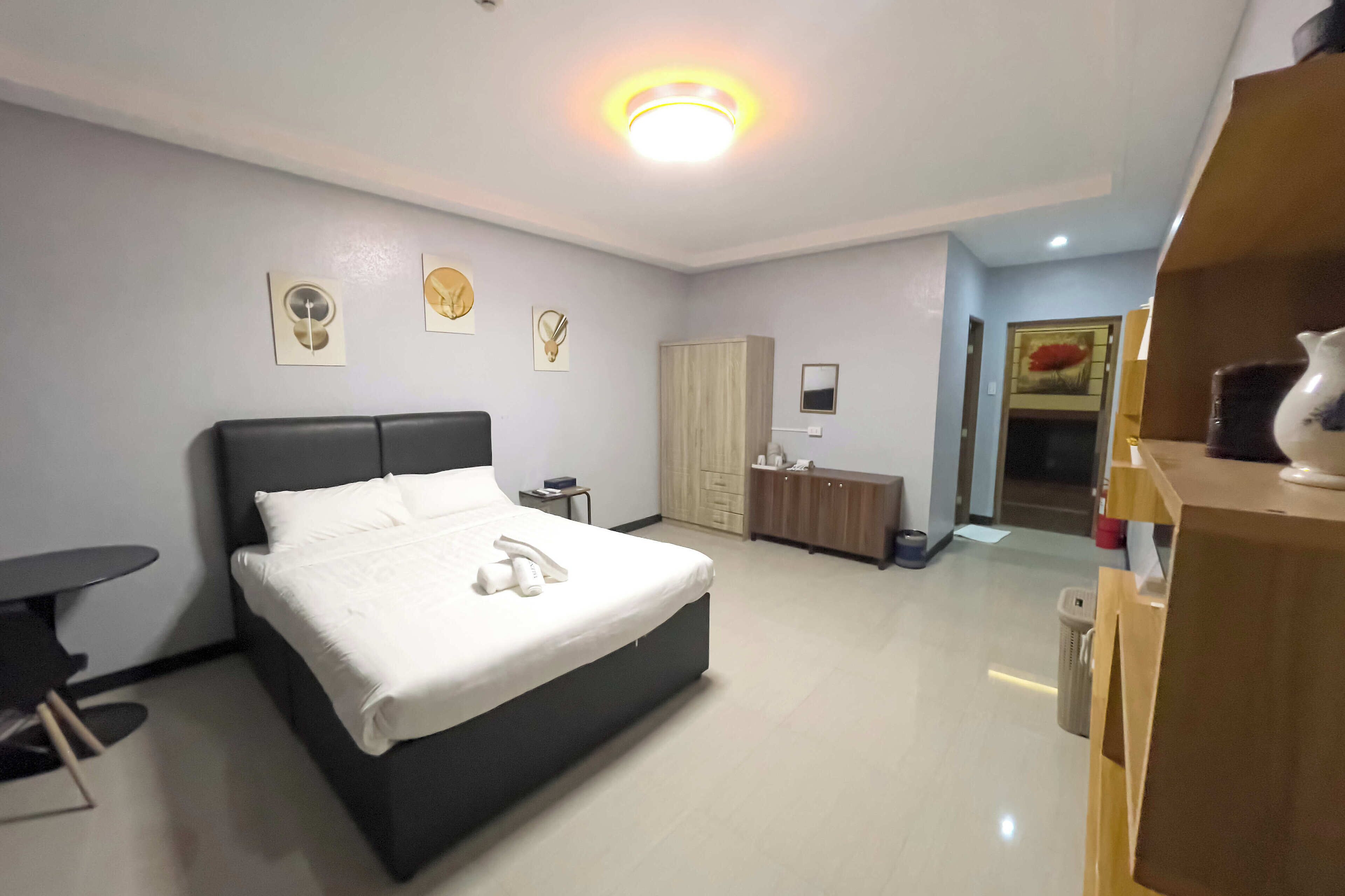 A modern hotel room with a large bed, bedside table, and a small desk.
