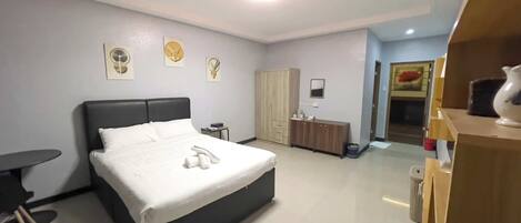 A modern hotel room with a large bed, bedside table, and a small desk.