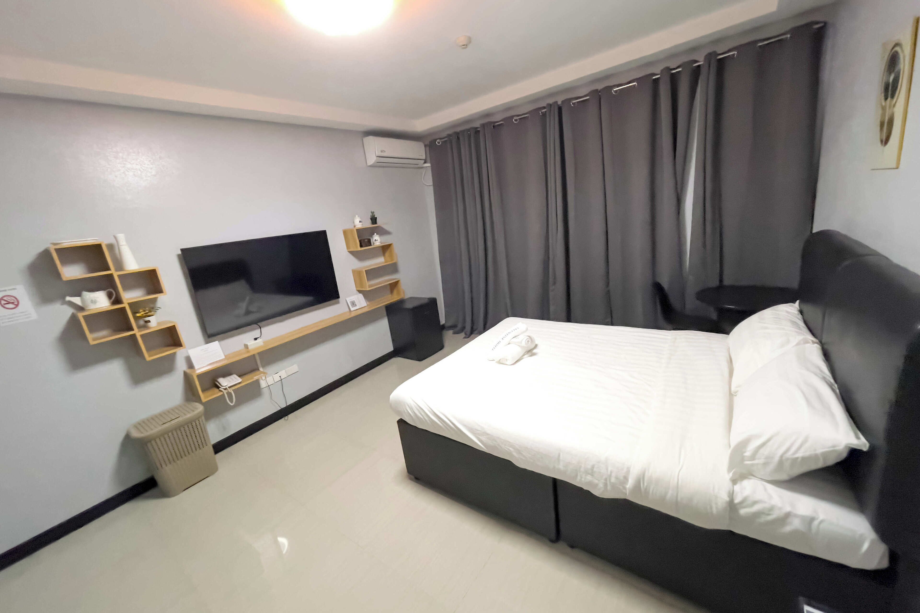 Habitación de hotel con cama, televisión y un pequeño estante con objetos.