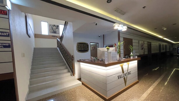 A hotel reception area with a staircase, a reception desk labeled "Valentine," and a sign indicating room rates. - Valentine Hotel Angeles City managed by Cocotel (Angeles City)