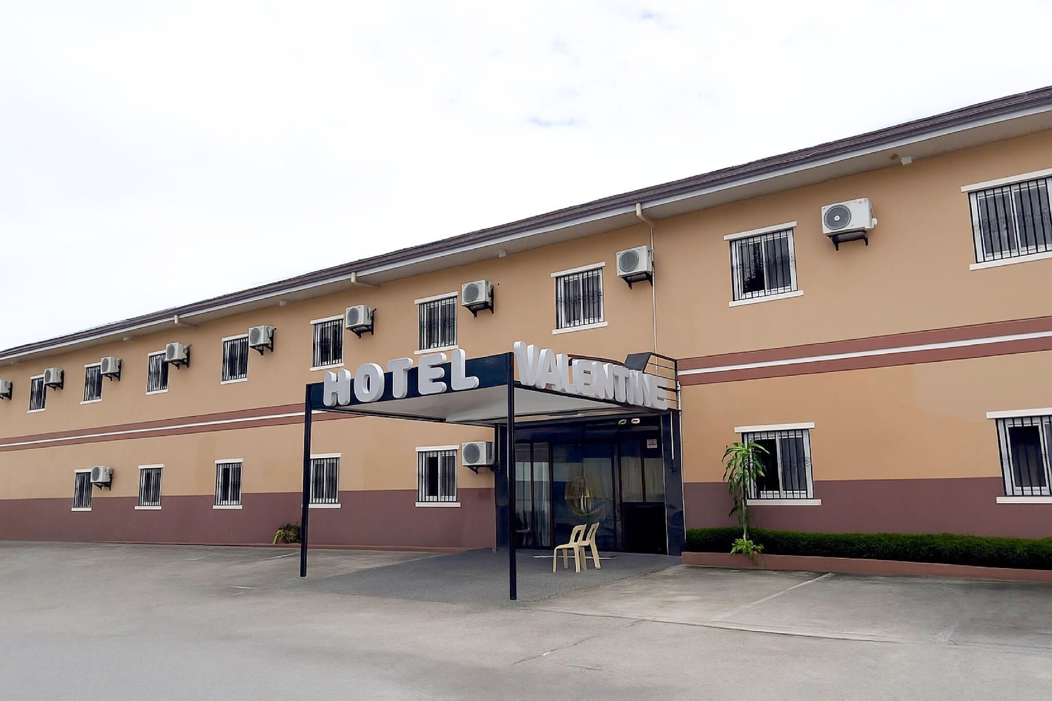 A hotel with a sign reading "HOTEL VALENTINE." It has multiple air conditioning units and windows with bars.