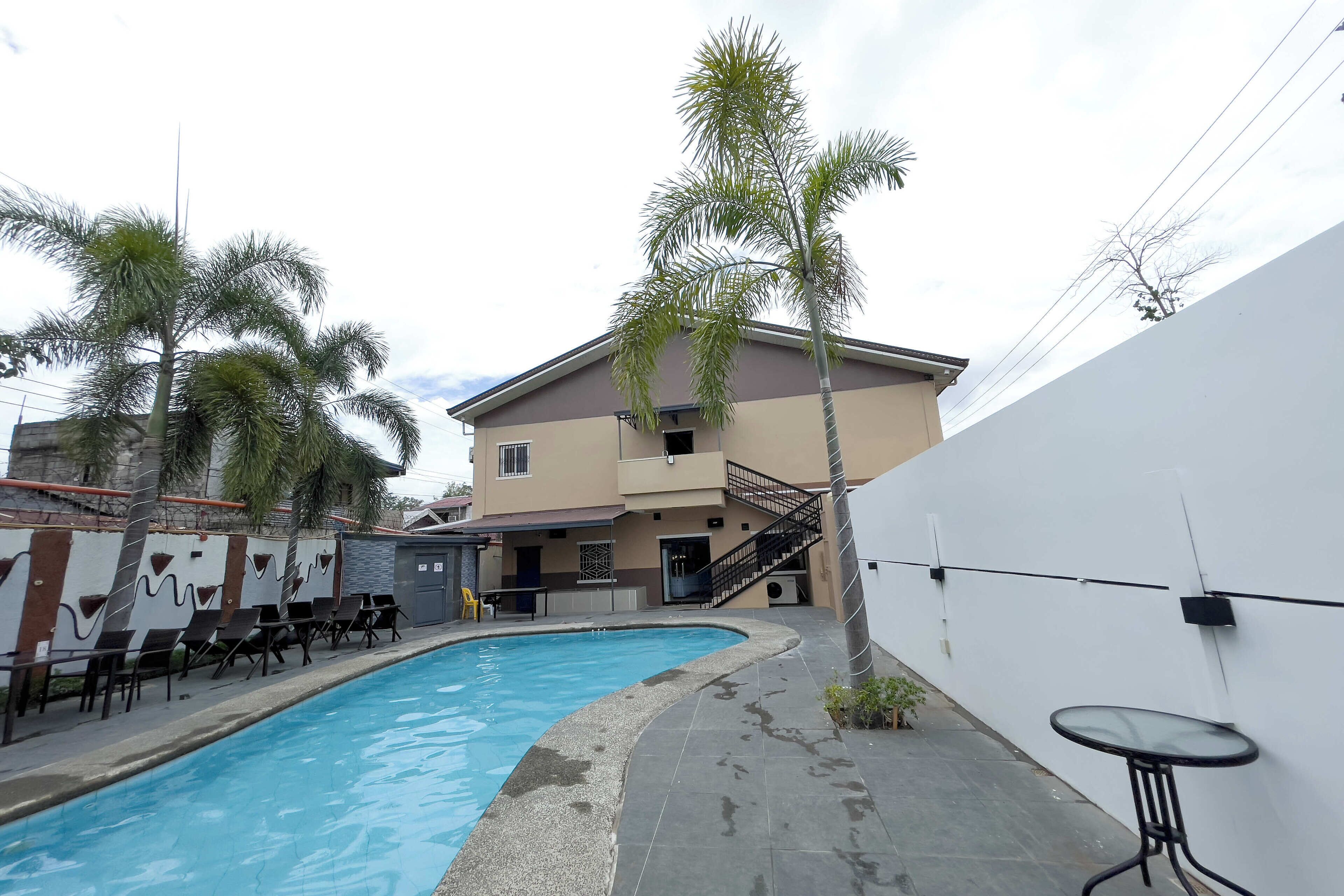 Una piscina con sillas de descanso, una mesita y una escalera que conduce a un edificio de fachada color crema.