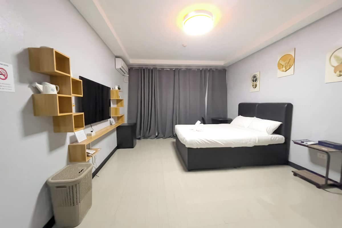 A hotel room with a bed, a TV on a shelf, a desk, and a wall-mounted air conditioner.