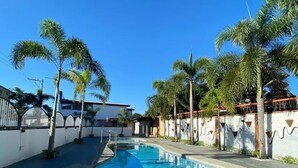 A swimming pool with a curved edge, surrounded by palm trees and a white wall with decorative elements. - Valentine Hotel Angeles City managed by Cocotel (Angeles City)