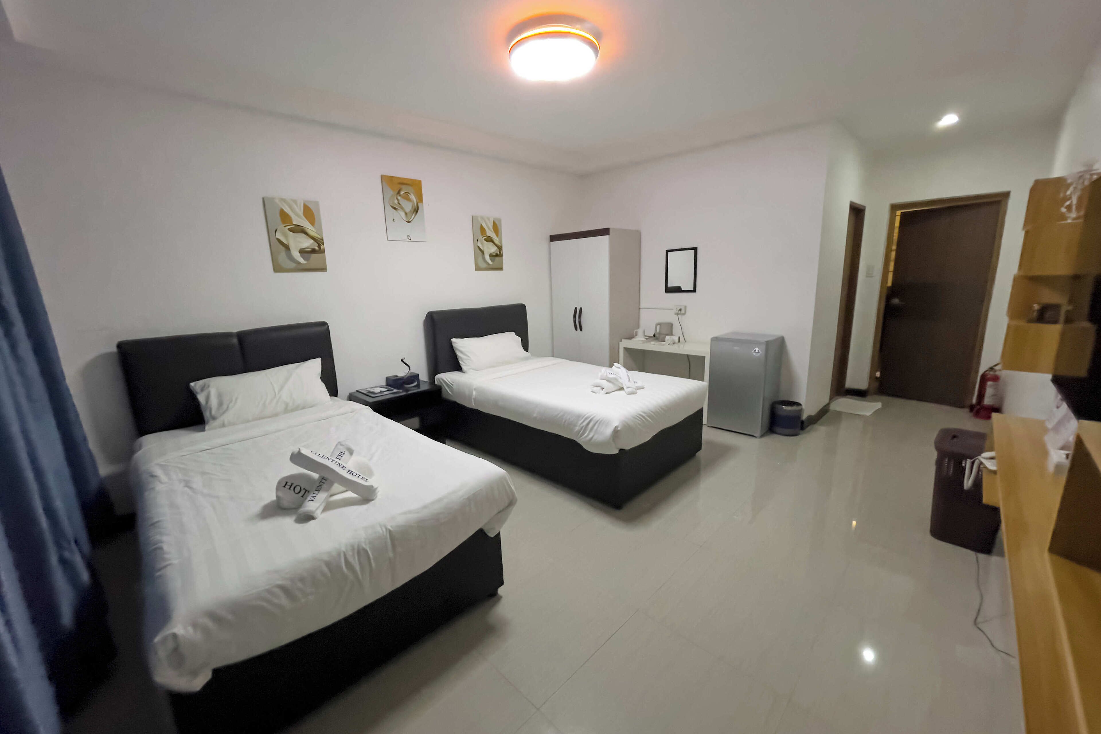 Una habitación de hotel con dos camas, un escritorio, un espejo y una pequeña kitchenette.