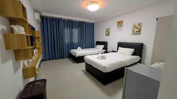 Habitación de hotel con dos camas, un escritorio, una silla, un cesto de basura y un estante en la pared con objetos.