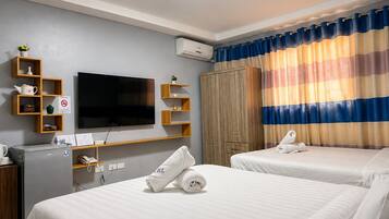 A hotel room with a flat-screen TV, wooden shelves, a wardrobe, and a striped curtain.