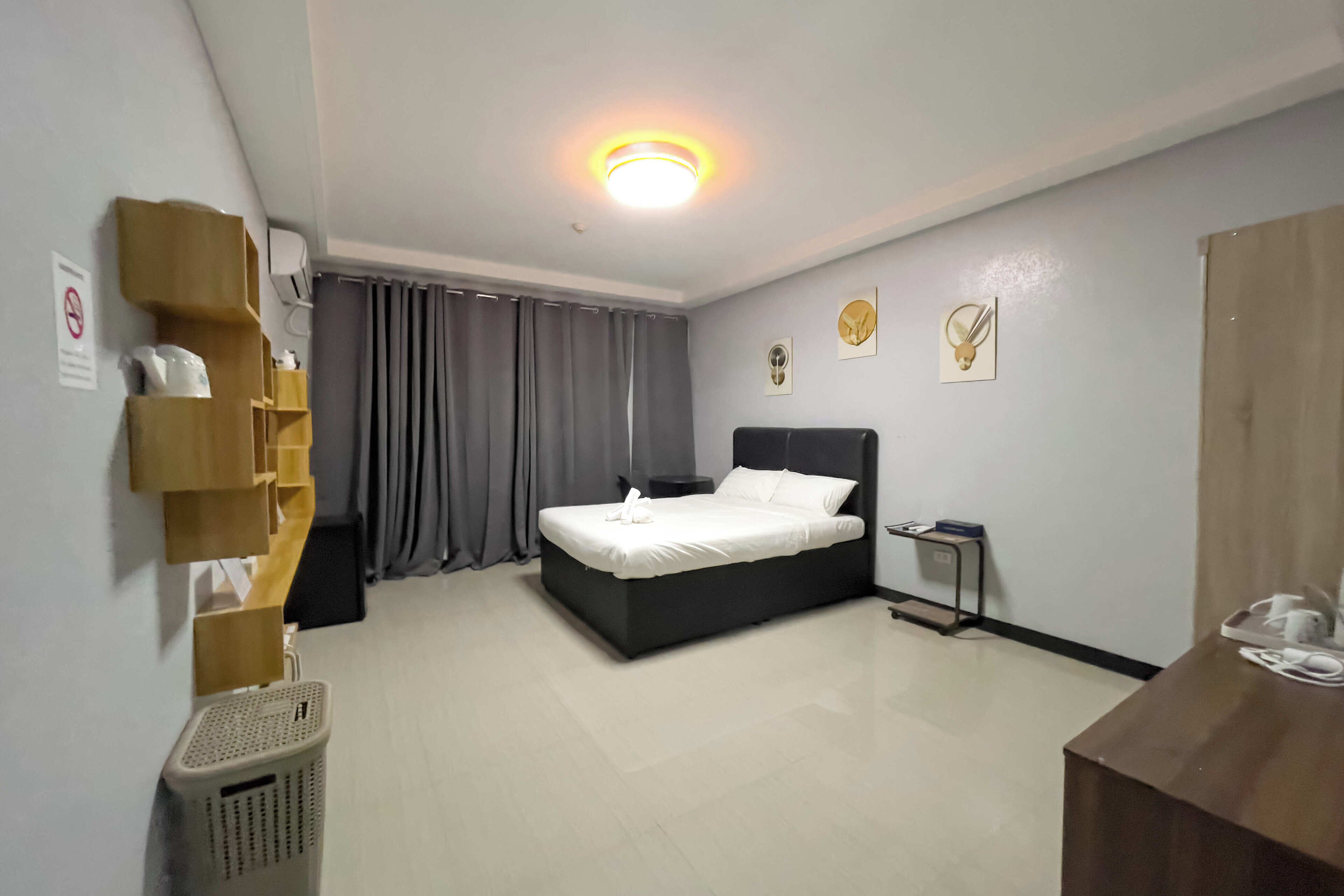Habitación de hotel con cama, escritorio, silla, cubo de basura y estante en la pared.