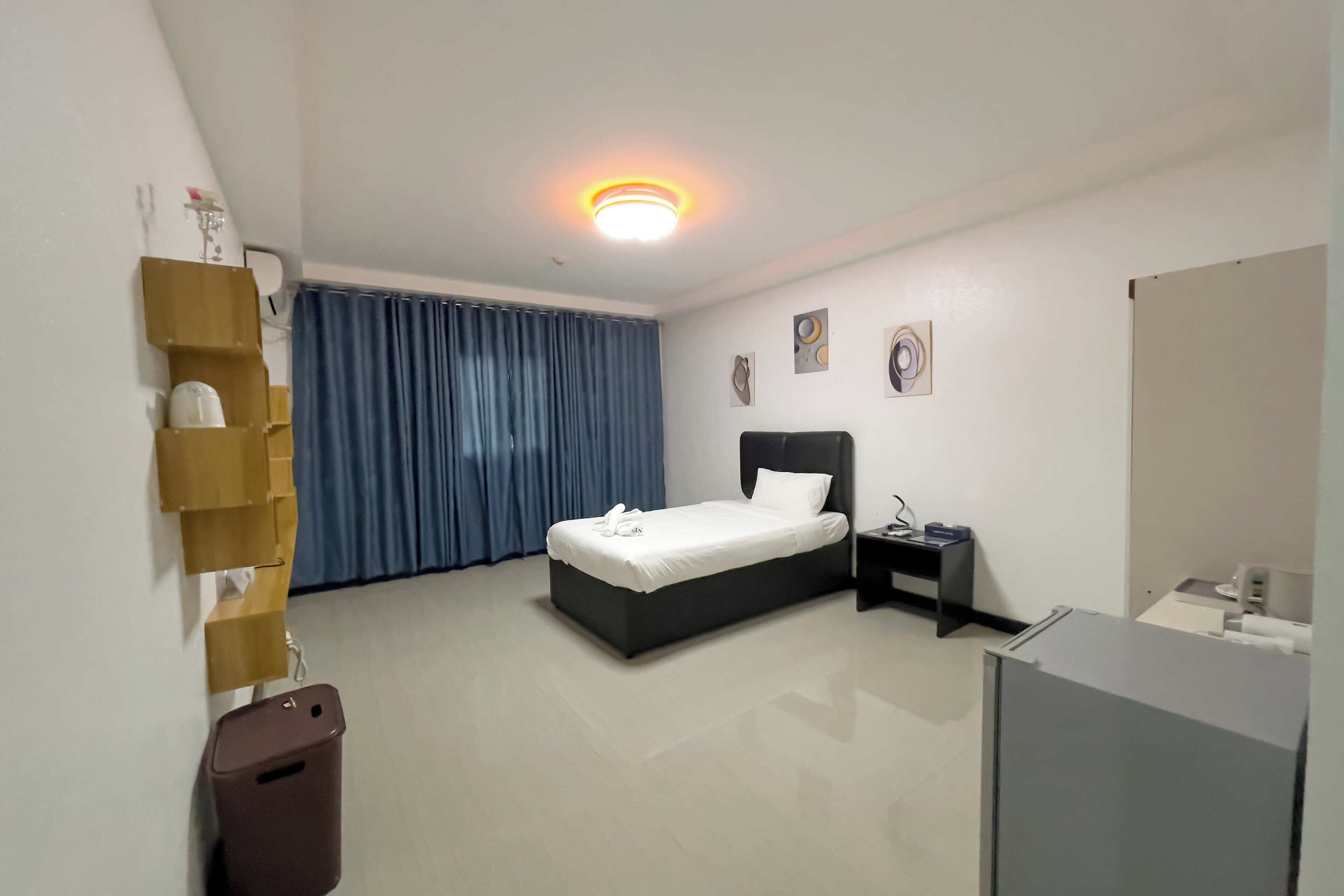 Une chambre d’hôtel comprenant un lit, une table de chevet, une poubelle, un bureau et un luminaire au plafond.