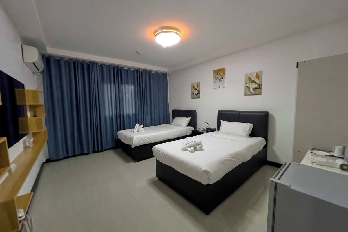 A hotel room with two beds, a desk, a chair, a lamp, and a window with curtains.