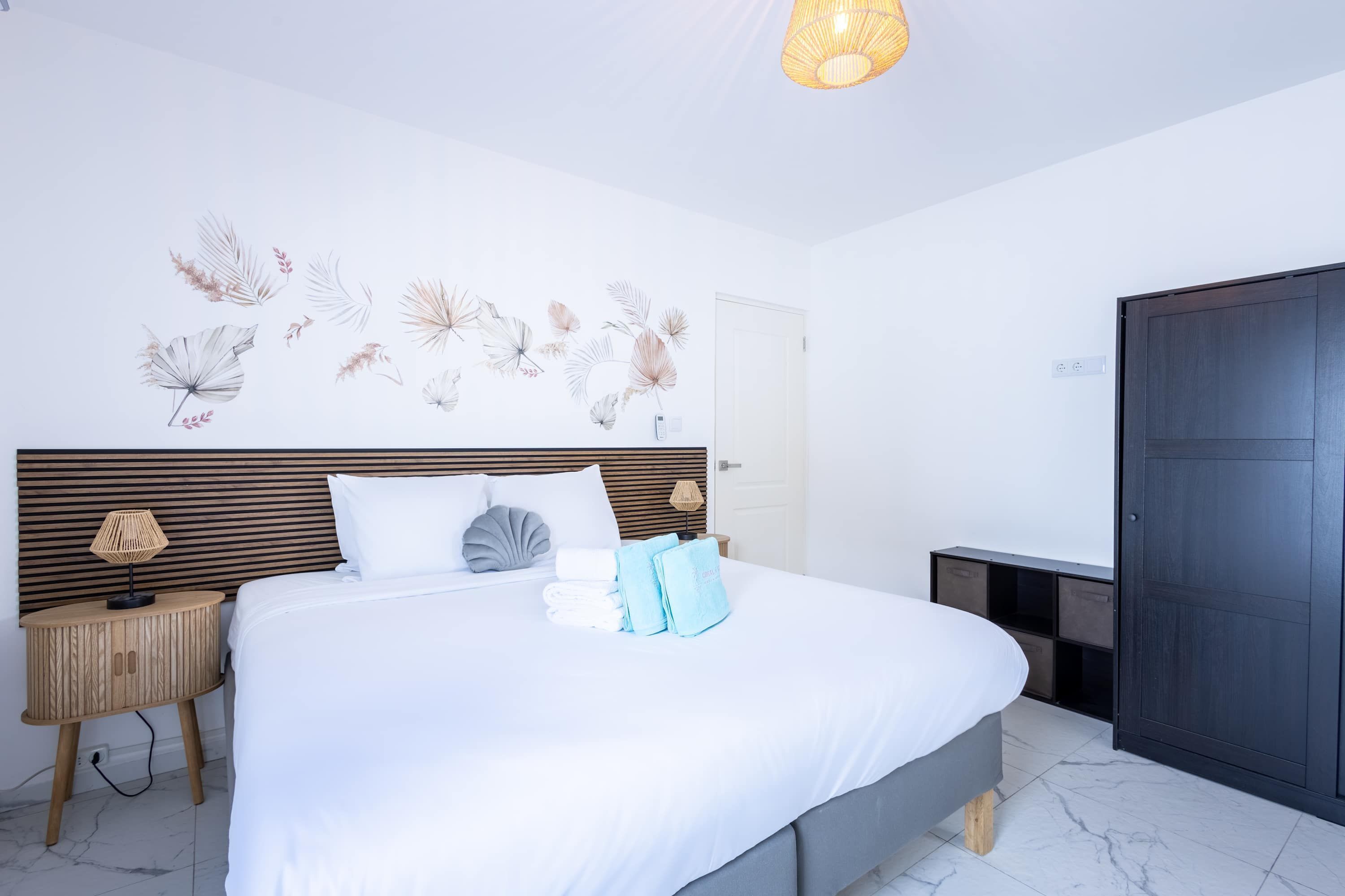 A neatly made bed with white linens, a wooden headboard, and a wall-mounted lamp.