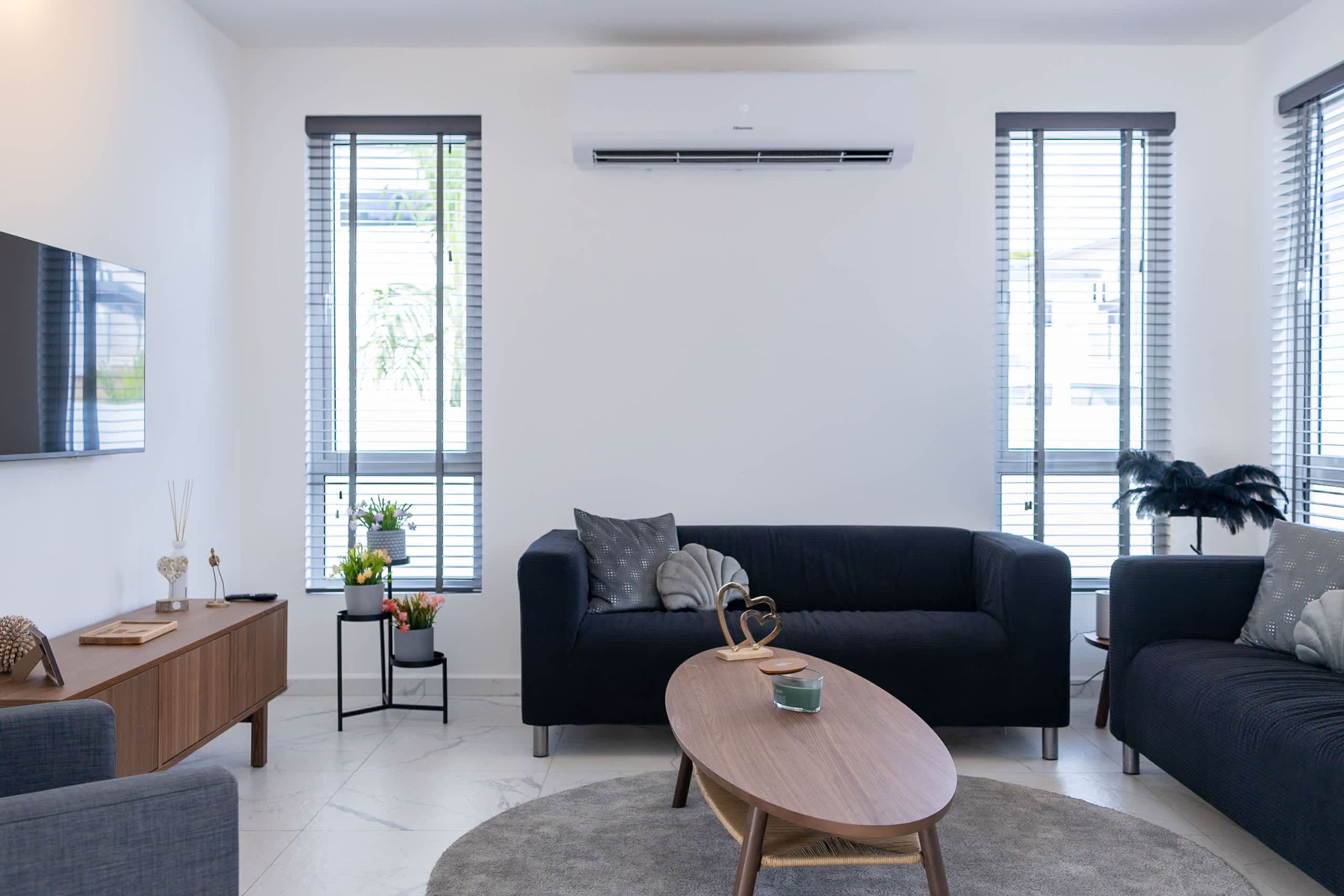 Un salon moderne avec un canapé foncé, une table basse en bois et un téléviseur fixé au mur.