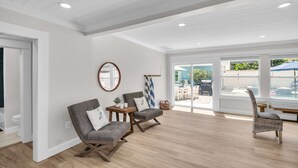 Una habitación amplia con suelo de madera, un gran ventanal con vistas al exterior, y dos sillones tapizados con una pequeña mesa y un espejo en la pared.