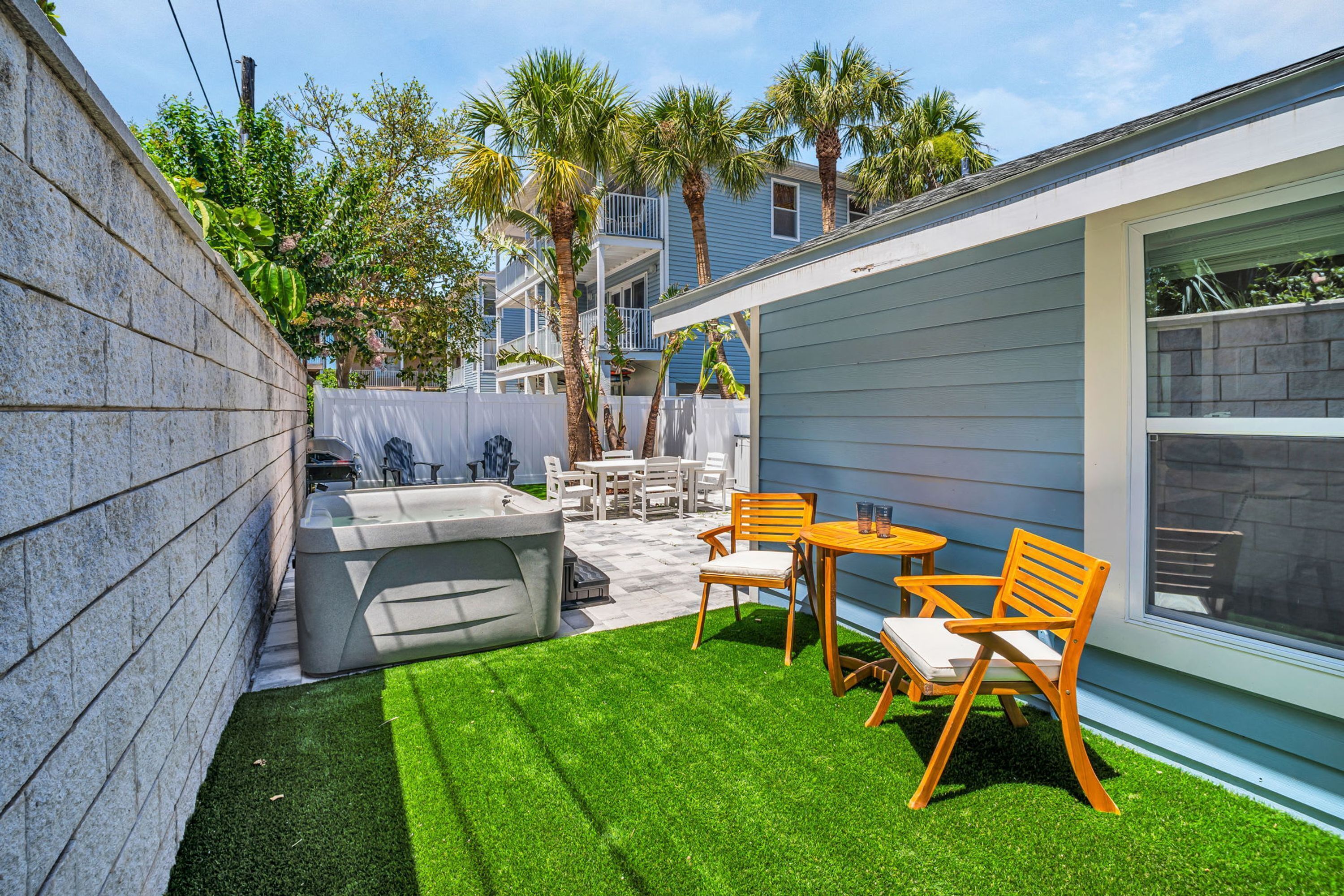 A backyard with artificial grass, a hot tub, and wooden chairs.