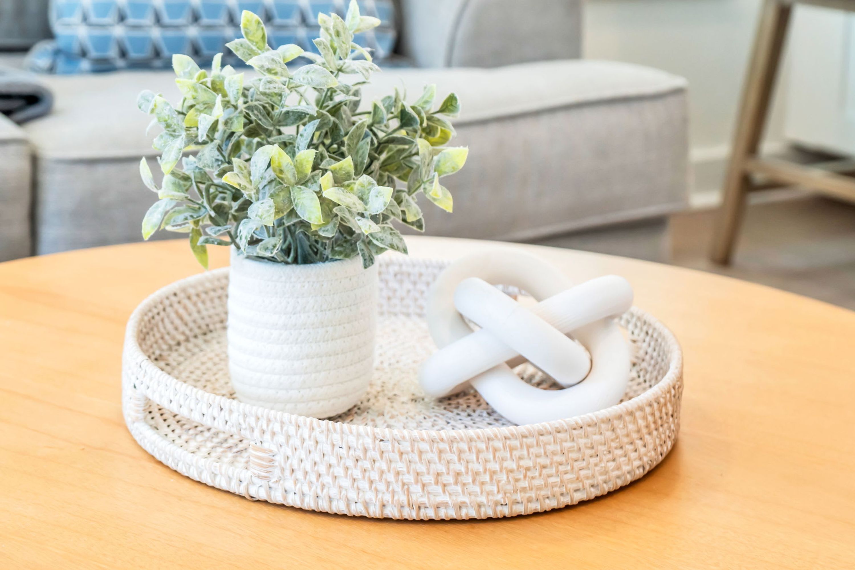 A woven tray with a white vase and a white twisted sculpture on a wooden table.