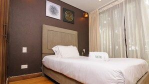 Een net opgemaakt bed met witte lakens en een kussen met de tekst 'OK', in een kamer met donkere muren, een houten hoofdbord en twee wandlampen.