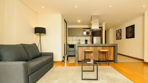Een moderne woonkamer met een grijze bank, een kleine tafel en een keuken op de achtergrond.
