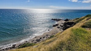 Un paisaje costero con un litoral rocoso, mar azul transparente y un acantilado cubierto de hierba.