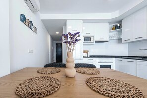 A modern kitchen with white cabinets, a central island with a vase of flowers, and a dining area with a wooden table and woven placemats.