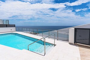 Piscina no terraço com vista para o oceano, guarda-corpo de vidro e design arquitetônico moderno.