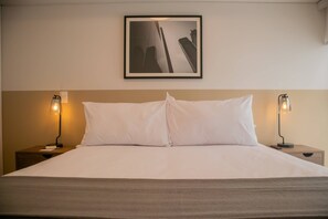 A neatly made bed with white linens, two bedside lamps, and a framed picture on the wall.
