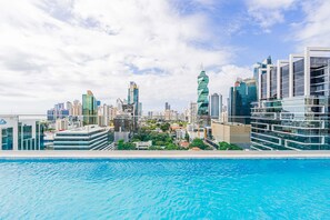 Un paisaje urbano moderno con un rascacielos prominente y retorcido, un gran edificio de cristal y una piscina en primer plano.