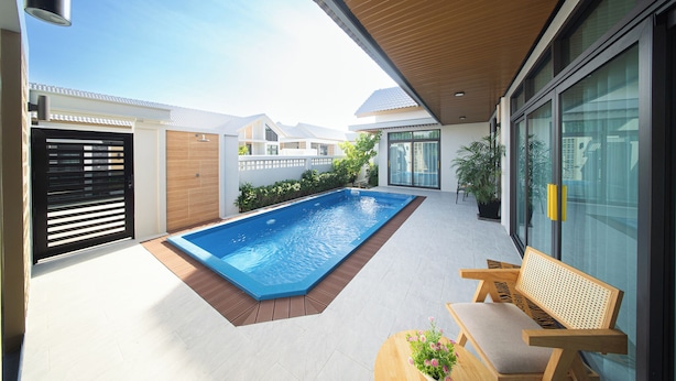 Un espace piscine extérieur moderne, doté d’une terrasse en bois, d’un banc et d’un mur en verre.